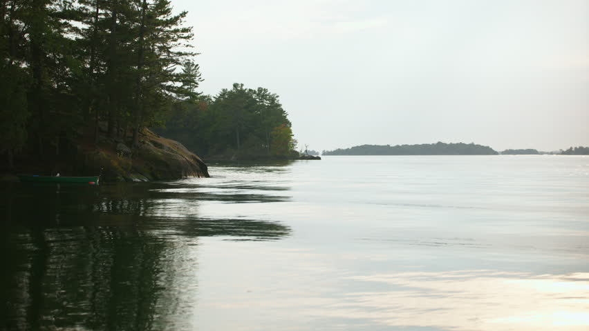 Handheld shot of a tranquil St. Lawrence River scene featuring a canoe by the rocky shoreline of Wellesley Island State Park in Fineview, NY.