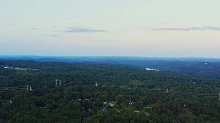 Drone fly-in capturing the expansive forests, rolling hills, and residential pockets of Yorktown Heights, NY. Scenic view with serene pastel skies at dusk.