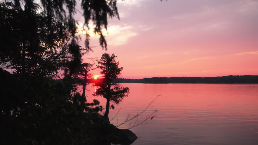 Static shot of a serene sunset reflecting vibrant pink and orange hues over the St. Lawrence River at Wellesley Island State Park, Fineview, NY.