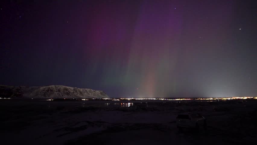 Time lapse wide shot of aurora borealis with Purple sky at night. Snowy mountains and driving cars on road.