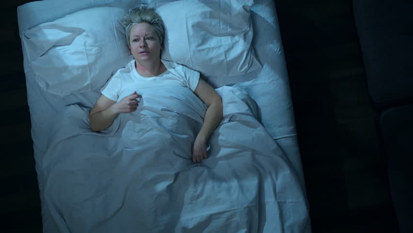 Annoyed woman can't sleep because of noise from neighbors while lying in bed in bedroom, top view.