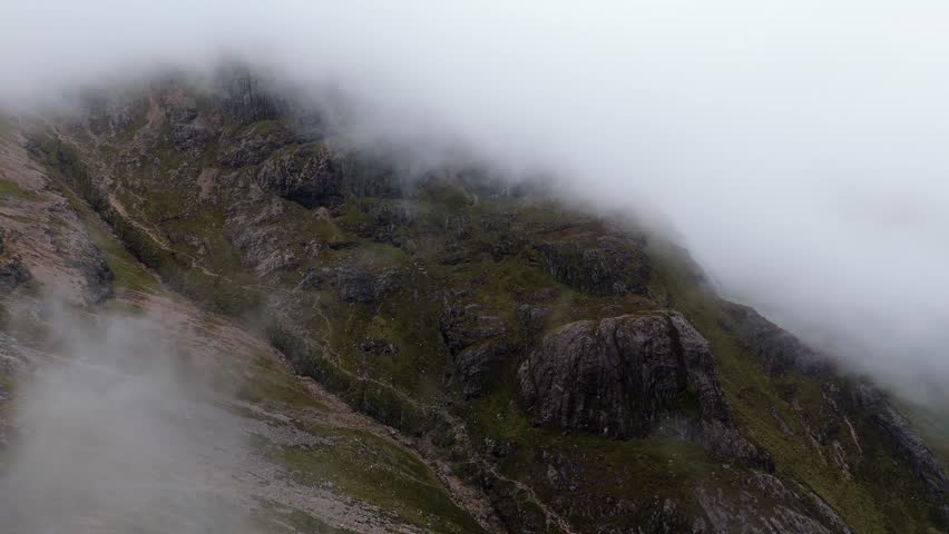 Aerial drone footage of the Glencoe mountain range showing a mountainside covered in mist and fog in the Scottish Highlands,