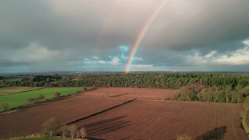 Wintertime sunny aerial drone flyover towards a beautiful double rainbow over the Cheshire countryside, UK