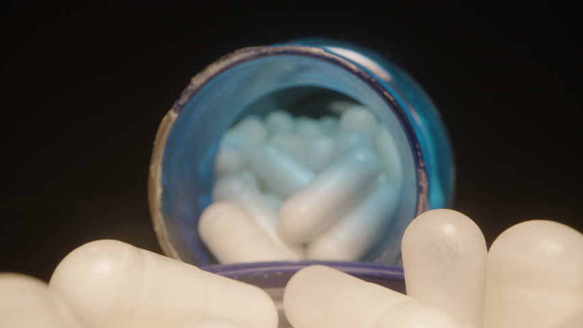 Fingers Picking a White Capsule from a Blue Lid with Blue Supplement Bottles in the Background, Illuminated in Detailed Dolly slider, close up.