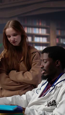 Vertical Video Multiethnic group of students in a library participate at a lesson with doctor, using medical books and materials to gain expertise in pharmacology and microbiology. Scientific studies