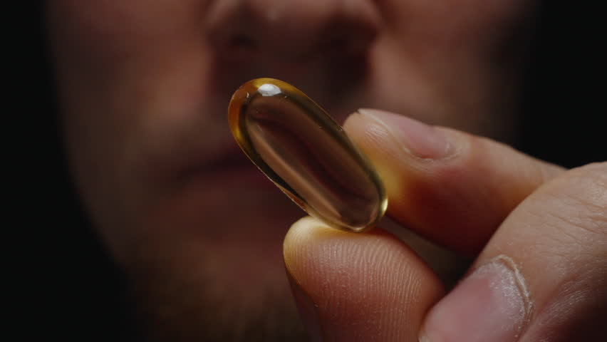 A Person Biting an Omega 3 Capsule Between Their Teeth Highlighting the Glossy Capsule and Facial Texture Nutritional Supplementation