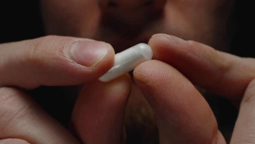 Hands Holding a White Capsule Between Fingers Highlighting Its Smooth Texture and Detail Against a Subtle Background Wellness and Healthcare