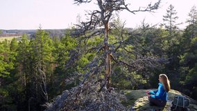 Young woman sitting in meditation pose on a mossy cliff surrounded by lush forest. Peaceful nature scene with sunlight filtering through trees. Mindfulness, solitude, mental well-being in outdoors. - Powered by Shutterstock - Get 15% off with code: PIKWIZARD15
