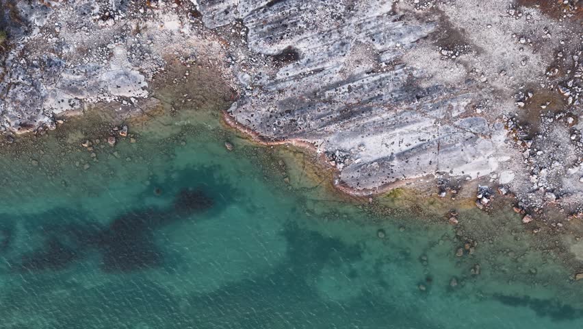 Aerial drone shot over crystal clear shoreline with rocky, textured terrain and vivid green water in Michigan’s Upper Peninsula
