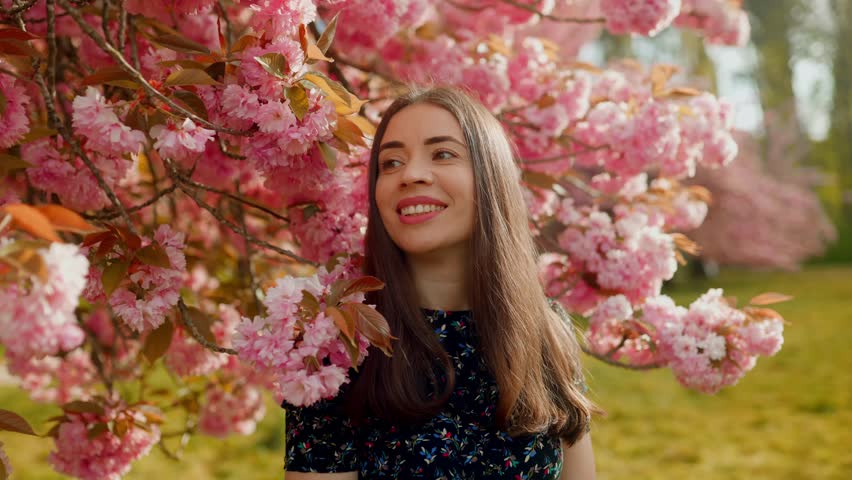 Beautiful young woman enjoying spring under blooming cherry blossoms. Sakura garden, peaceful nature, floral scene, seasonal beauty, springtime vibes, feminine serenity, pink flowers, slow motion, out