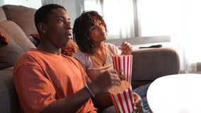 Young african american couple sharing intimate movie night, lounging comfortably on sofa while eating popcorn and enjoying film together with genuine connection and laughter - Powered by Shutterstock - Get 15% off with code: PIKWIZARD15
