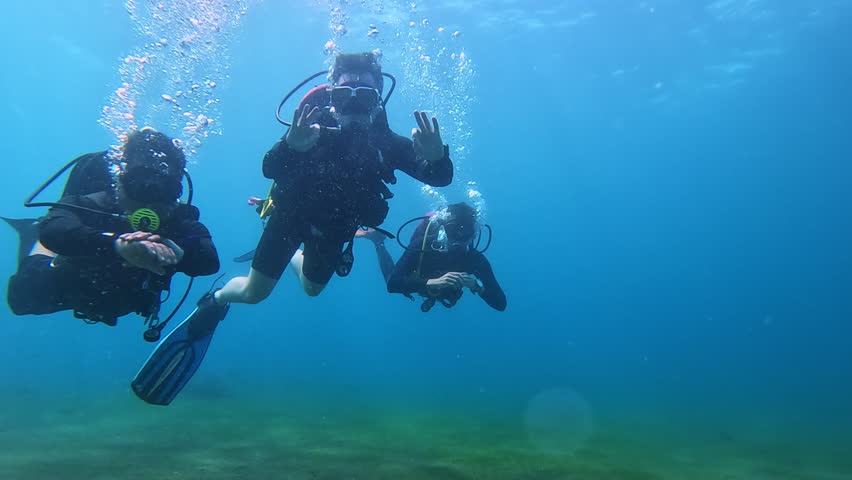 Divers with rising bubbles show OK gesture in clear ocean water. Positive sportsmen with scuba masks dive enjoying underwater journey on vacation. Extreme sports