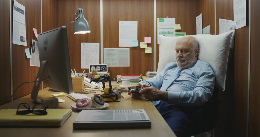 Lazy office worker sitting at his desk and playing instead of working, he is picking up a donut using a toy robotic arm