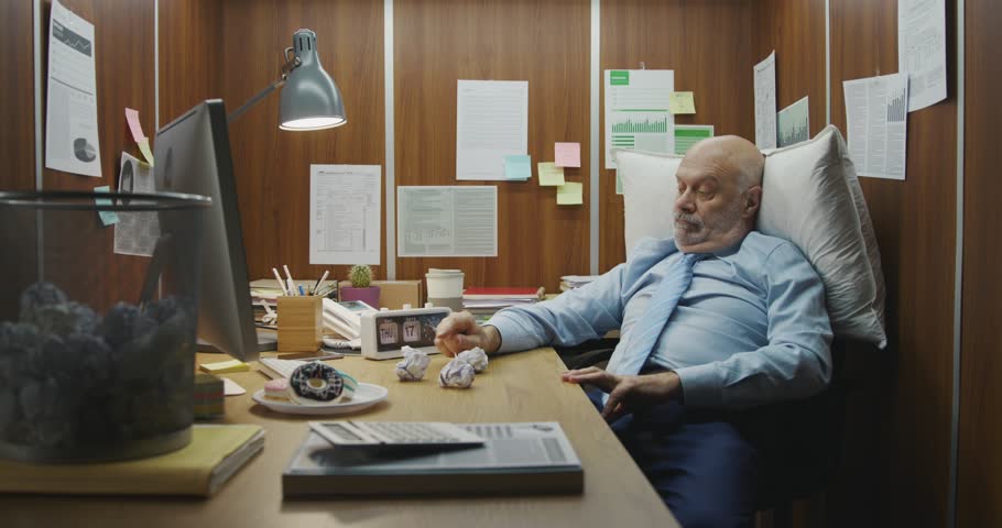 Bored lazy office worker sitting at his desk, he is throwing crumpled paper in the trash bin and wasting time instead of working