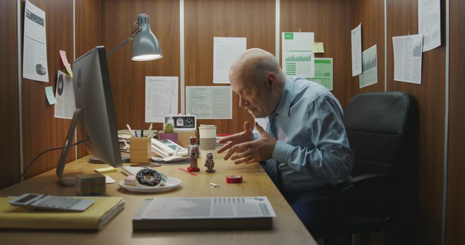 Funny lazy businessman sitting at his desk in a tiny office, he is playing with vintage tin toy robots instead of working