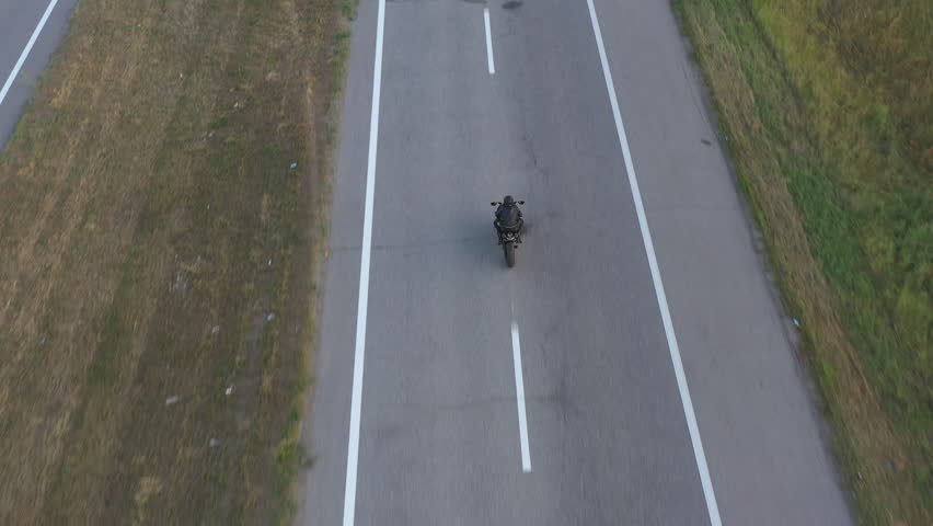 Top view to biker driving motorbike during road trip. Man ride fast on modern sport motorcycle at highway. Motorcyclist racing his bike on country road. Concept of journey and adventure. Aerial shot