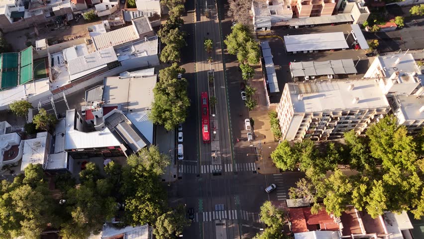 Red tram driving along roads of Mendoza city at sunset, Argentina. Aerial top-down view