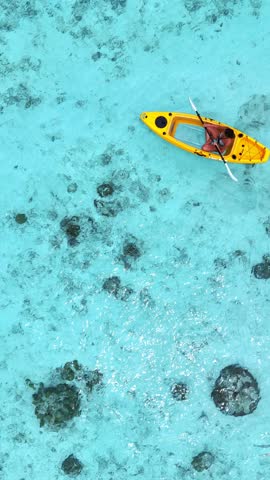 woman in a bikini relaxes on a yellow kayak floating on clear turquoise sea, top-down view from above, peaceful moment in tropical paradise, summer holiday, maldives, travel, holidays, vacation