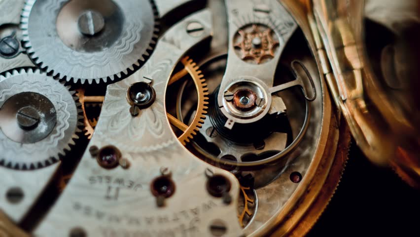 Camera zooms in on a vintage pocket watch mechanism, revealing ornate gears and polished surfaces. The slow-motion macro footage highlights every intricate detail of the antique design.