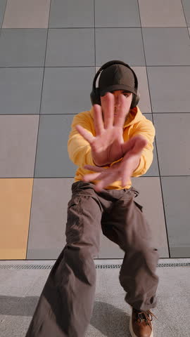 Male dancer showcasing bold freestyle move near architectural tiles in vertical video. Urban fashion, dynamic attitude, city energy, youth expression, casual choreography style. Freedom
