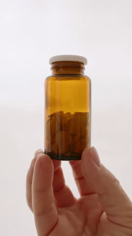 Vertical brown glass bottle filled with pills woman hand holding, healthcare, supplements wellness. Minimalist background emphasizes focus health products medication management. Self-care. Lifestyle