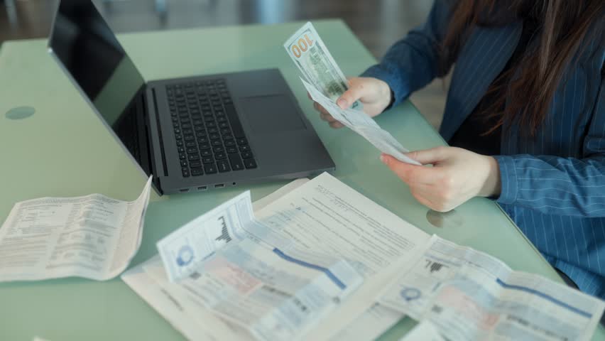 Pile of cash, receipts, and bills laid out on a desk with a laptop. Financial planning, expense tracking, and the stress of paying multiple obligations.