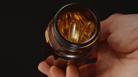Hand Pouring Omega 3 Capsules from a Brown Glass Bottle into an Open Palm, Capturing the Motion Against a Dark Background - Powered by Shutterstock - Get 15% off with code: PIKWIZARD15