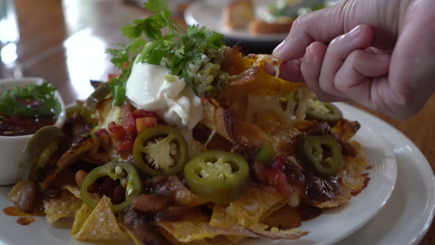 hand eating mexican food cheesy nachos plate with beef salsa jalapeno and sour cream