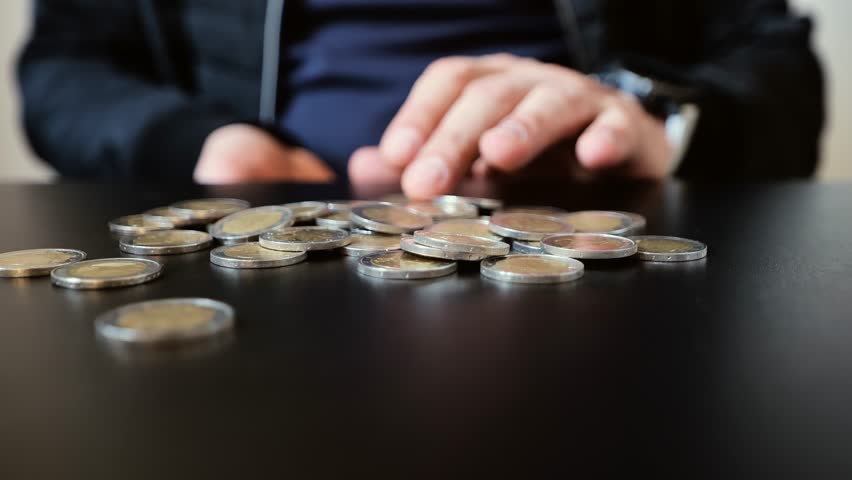 Detailed slow motion of fingers moving coins, black surface, representing money