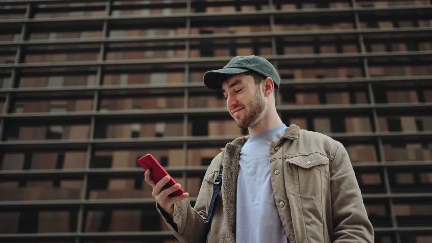 Young man using mobile phone in the city, in front of modern corporate urban office building