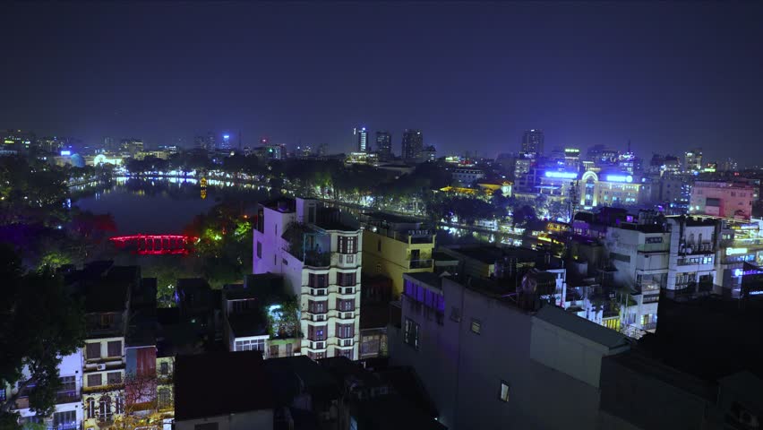 Hanoi City Old Quarters Lake at night glowing with vibrant colourful city lights surrounded by old historic buildings small bridge crossing the lake Hanoi Vietnam