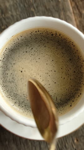 Vertical video. Hand stirring sugar in cup of espresso coffee. Morning routine.
