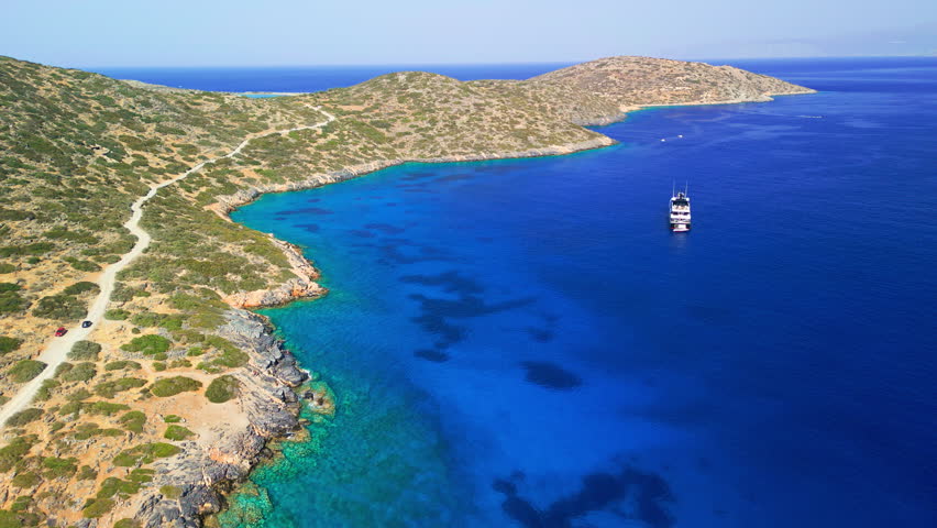 High angle view of a yacht in a blue bay along the rocky coast of Crete, Greece.