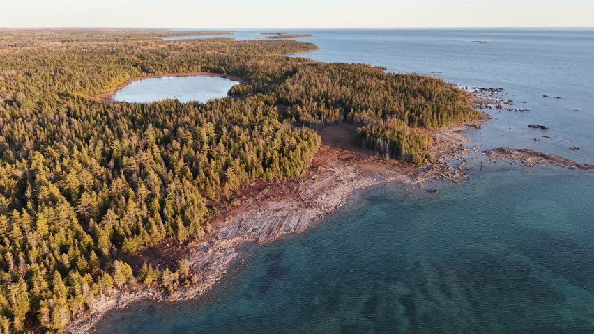 Drone footage of Lake Huron coastline with forested land, rocky shoreline, and clear blue water in Michigan’s Upper Peninsula