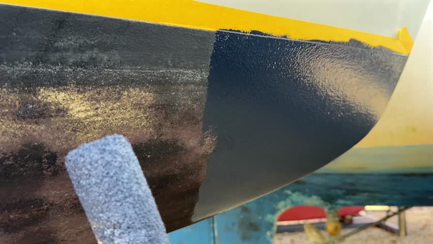 Applying antifouling paint to sailboat hull with roller brush