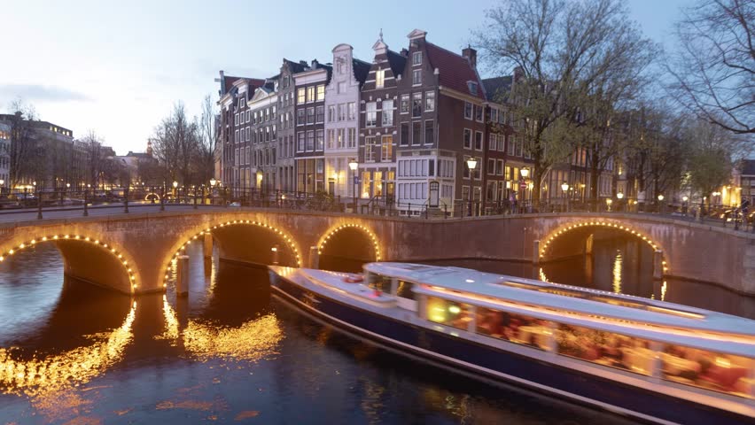 Amsterdam historic city centre evening Timelapse, canal bridges illuminated at night. The Keizersgracht and Reguliersgracht intersection with night illumination, reflection in the canals 