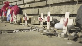 Small wooden crosses with pink hearts and poppy wreaths rest at the base of a brick war memorial - Powered by Shutterstock - Get 15% off with code: PIKWIZARD15
