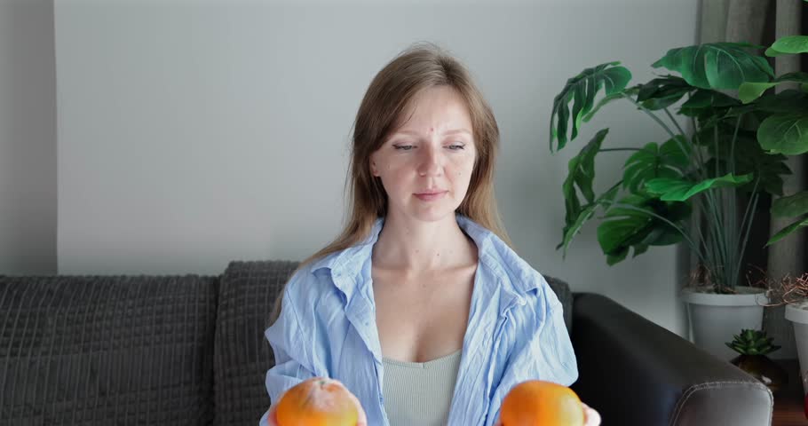 Woman evaluating two oranges on sofa, food choice concept, fresh produce selection, nutrition and healthy eating theme.