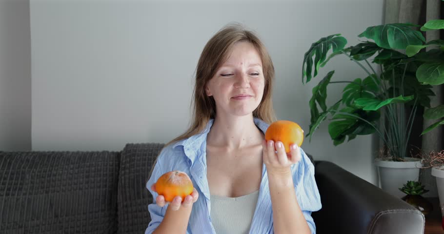 Woman evaluating two oranges on sofa, food choice concept, fresh produce selection, nutrition and healthy eating theme.