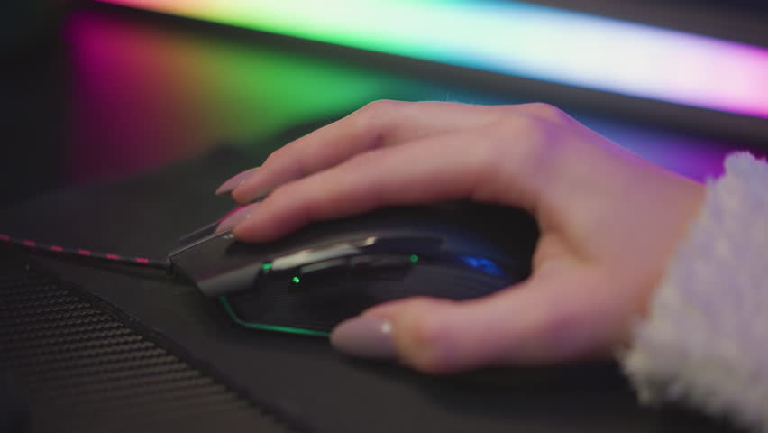 Close up of woman hand with polished nail in fluffy sweater gripping gaming mouse on black pad under vibrant rgb ambient strip lighting, soft focus background