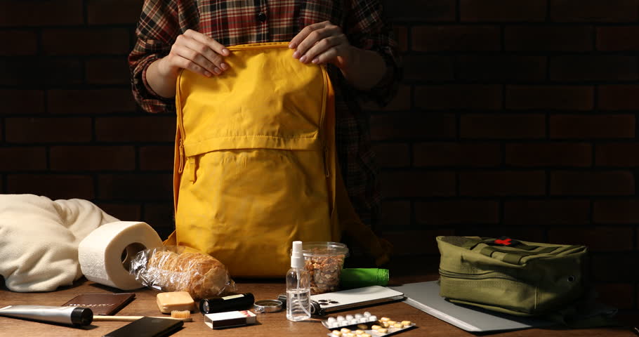 Survival kit. Woman packing different emergency supplies at wooden table indoors, closeup