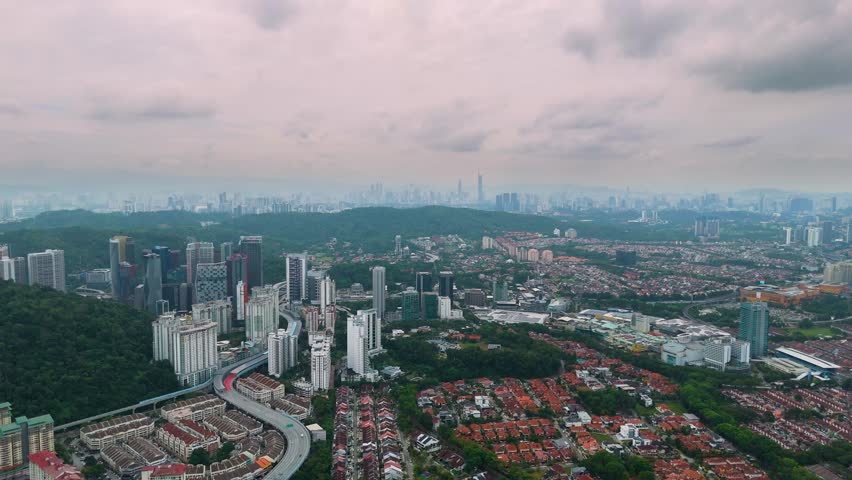 Expansive aerial view of Kuala Lumpur and Petaling Jaya cityscape under a cloudy sky, showing urban density, high-rise buildings, residential zones, and surrounding hills. UHD.