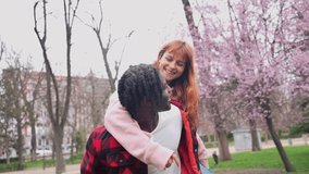 Joyful interracial couple enjoying playful piggyback ride amid blooming park trees during vibrant spring day, showcasing youthful love and carefree connection - Powered by Shutterstock - Get 15% off with code: PIKWIZARD15