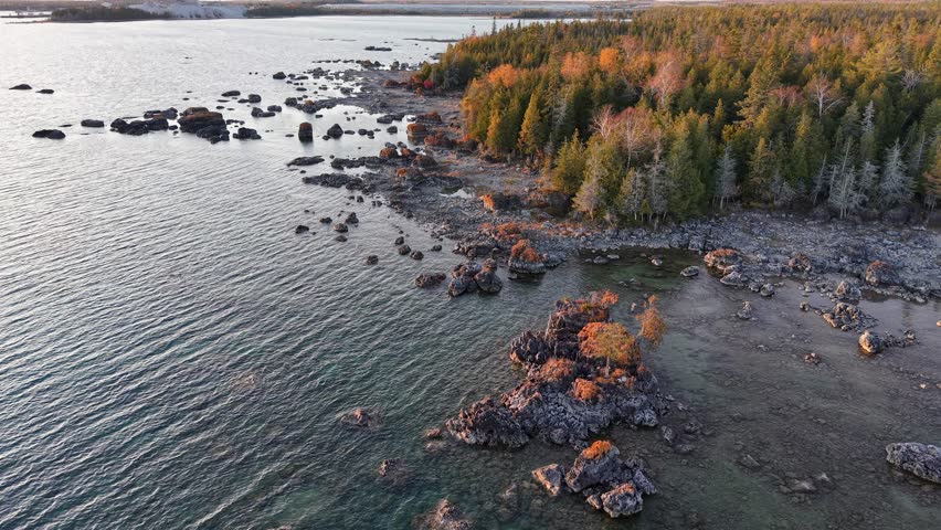 Drone footage over rocky Lake Huron shoreline framed by colorful autumn trees in Michigan’s Upper Peninsula