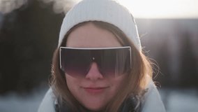 Young woman adjusting tinted goggles over white beanie with blissful smile and wind and blown hair against snowy urban skyline under bright winter sunshine glinting off frosted streets - Powered by Shutterstock - Get 15% off with code: PIKWIZARD15
