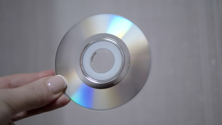 A hand holds a CD, showcasing its iridescent surface and reflecting light. Great for technology, music, or data-related projects.