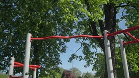 Athletic man performing pull-ups on red horizontal bar in park. Athlete training upper body muscles on outdoor gym. Person doing strength workouts. Concept of sports, fitness and healthy lifestyle - Powered by Shutterstock - Get 15% off with code: PIKWIZARD15