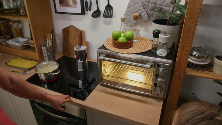 Medium high-angle shot of father opening oven door, and young daughter placing cupcake or muffin tray with batter inside, while baking together at weekend in kitchen of family home
