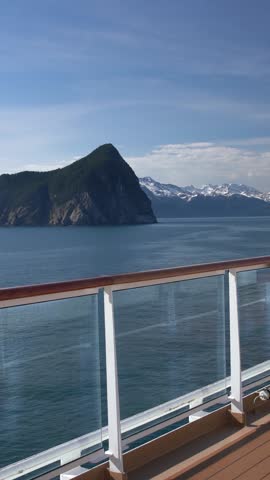 Vertical video of leaving Seward Alaska on cruise with man entering frame and pan across the scenery from deck