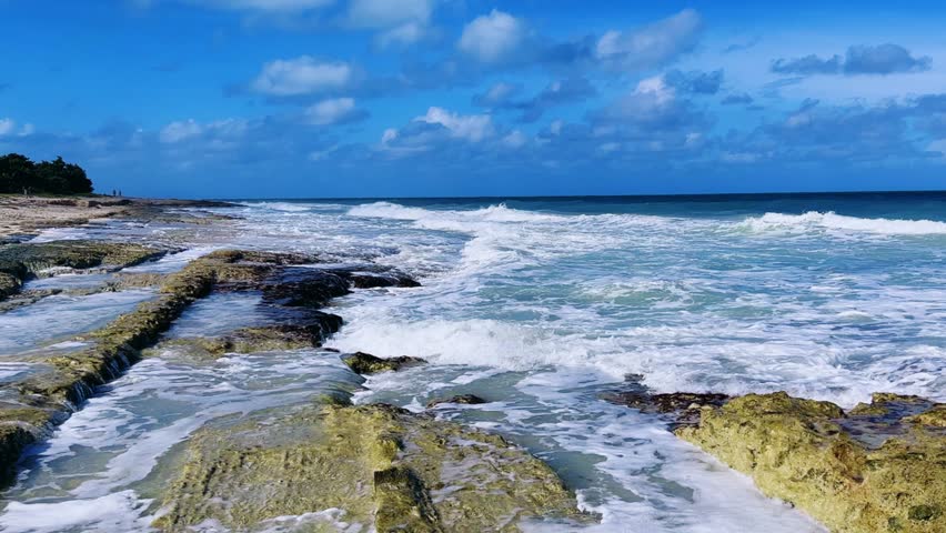 Rocky Cuban beach in Varadero, Cuba, on a cloudy day, when the sun breaks through the clouds, you can see the waves and ocean expanses. Turquoise waves. Stone slabs on the beach in the ocean. 4K	